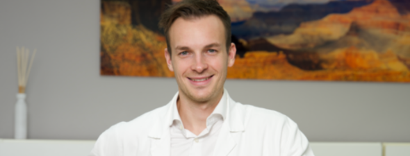 Smiling man in white shirt sitting in front of an abstract painting.